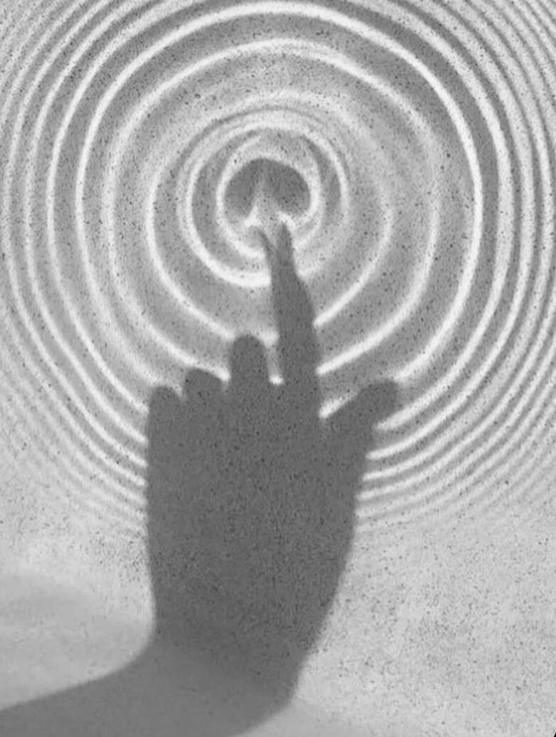 Black-and-white photograph of a hand touching rippled sand